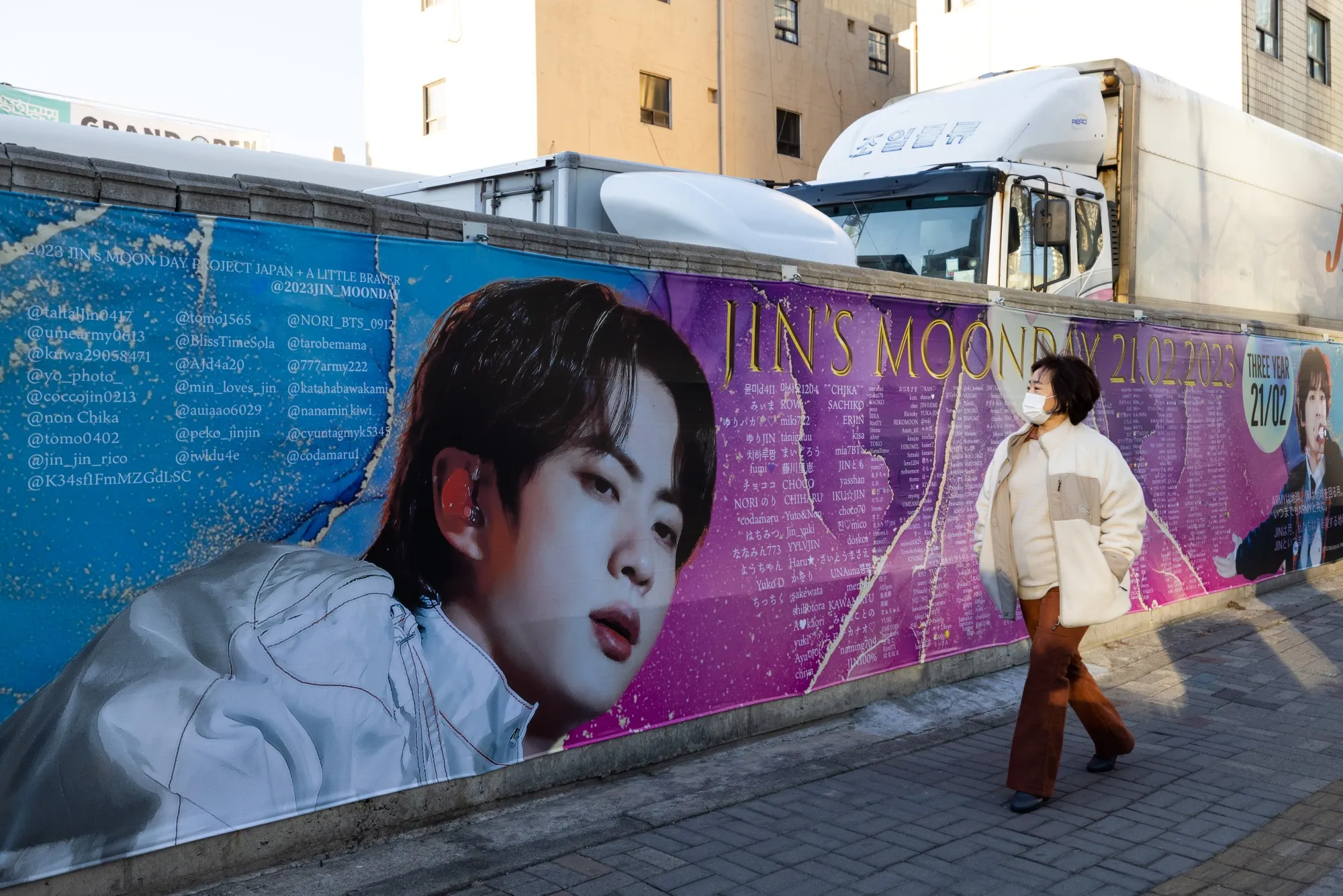 A woman walks past the photograph of Jin, a member of K-pop boy band BTS.