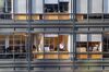 Daytime view of six windows of a glass-and-steel office building with individual workers framed in the two separate rooms.