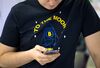 An attendee wearing a t-shirt decorated with a bitcoin rocket illustration and the words 'To the Moon' checks his smartphone at the CrytoSpace conference.