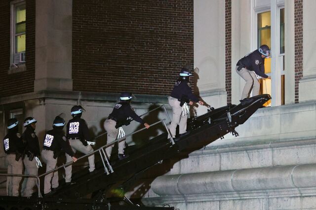 Police officers are climbing up a mechanical staircase to the second floor of a university building and opening a window to get inside.