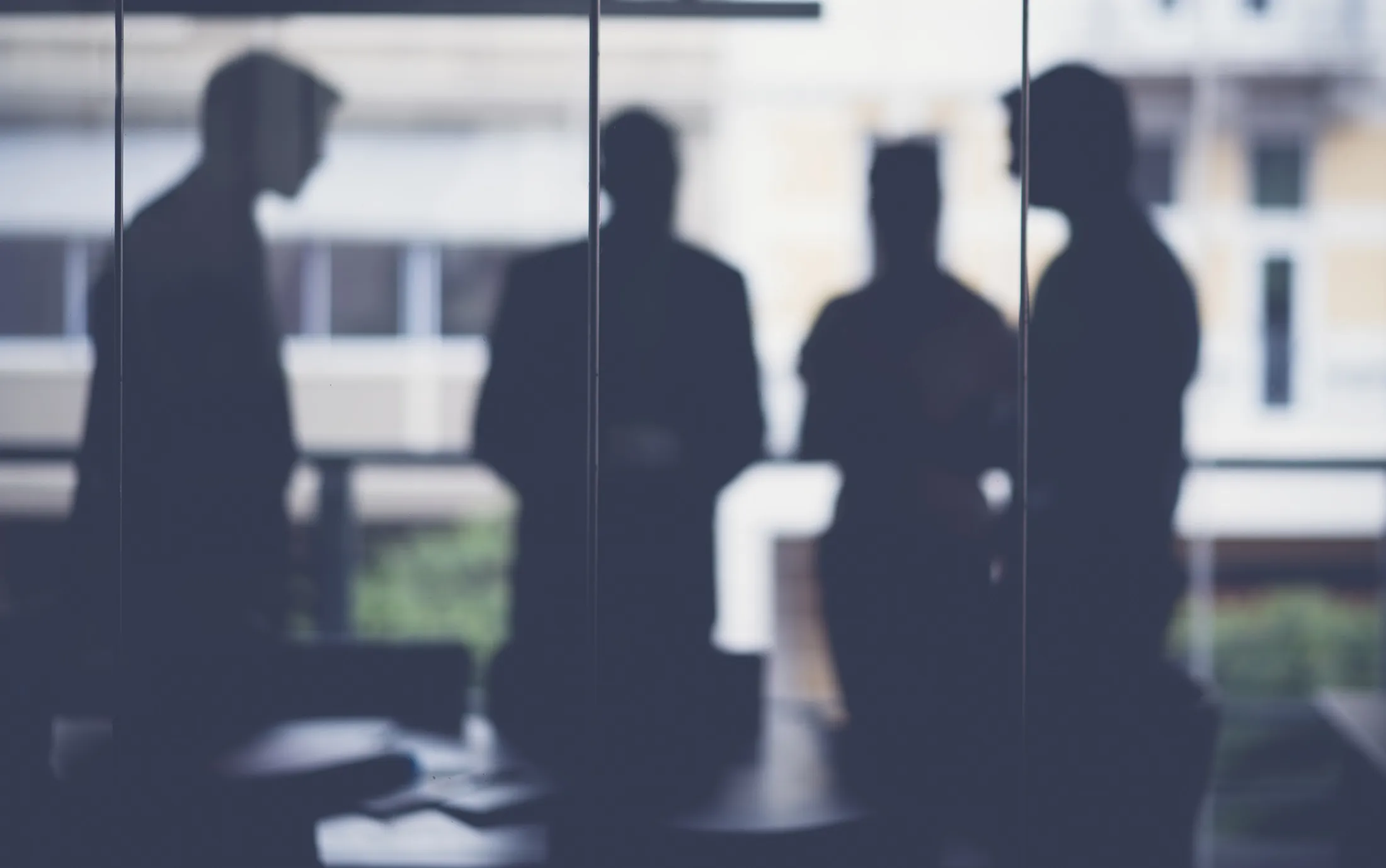 A photo of silhouette business people in meeting room. Male and female colleagues discussing at table. They are in modern glass office.