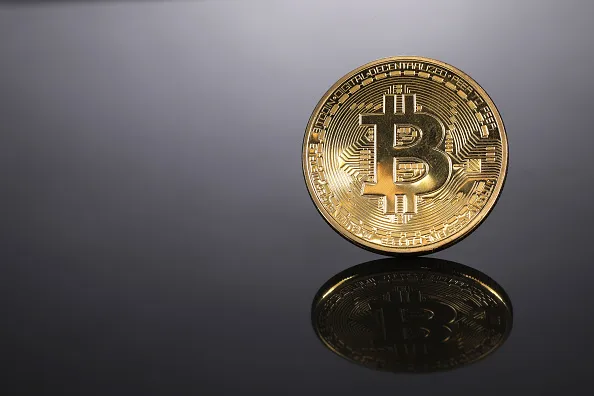 A coin representing Bitcoin cryptocurrency is reflected on a polished surface as it sits in this arranged photograph in London, U.K., on Thursday, Feb. 8, 2018.&nbsp;Canadian investment manager&nbsp;Ninepoint Partners LP&nbsp;completed a C$230 million ($180 million) initial public offering, the country’s largest new fund to be based on the cryptocurrency.