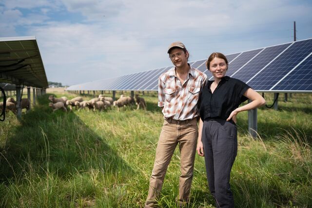 Arlo Hark and Josephine Trople stand for a portrait in front of solar panels at their farm. 
