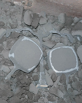 Cast iron skillets exit the forging process and run along a conveyor belt as excess material is shaken loose