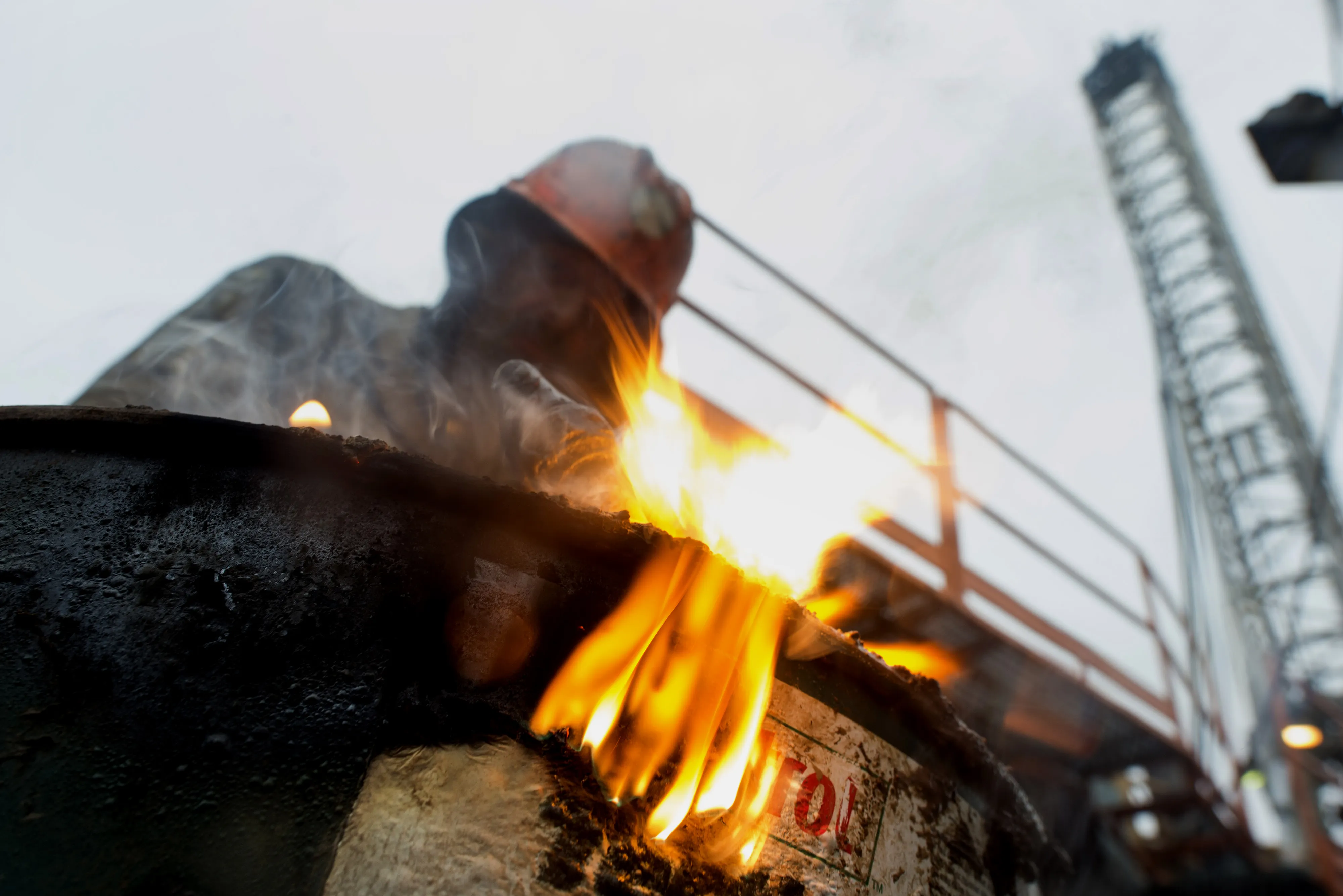 A drill pusher uses a torch to cut the top off a 50-gallon metal drum on an oil drilling site.
