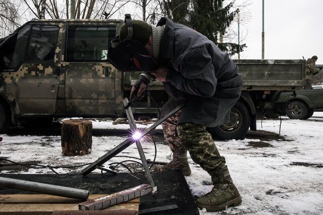 Members of the 242 Territorial Defense battalion are slicing and welding steel pipes to fit swivel mounts for machine guns on top of pickup trucks, oriented vertically to shoot down drones.