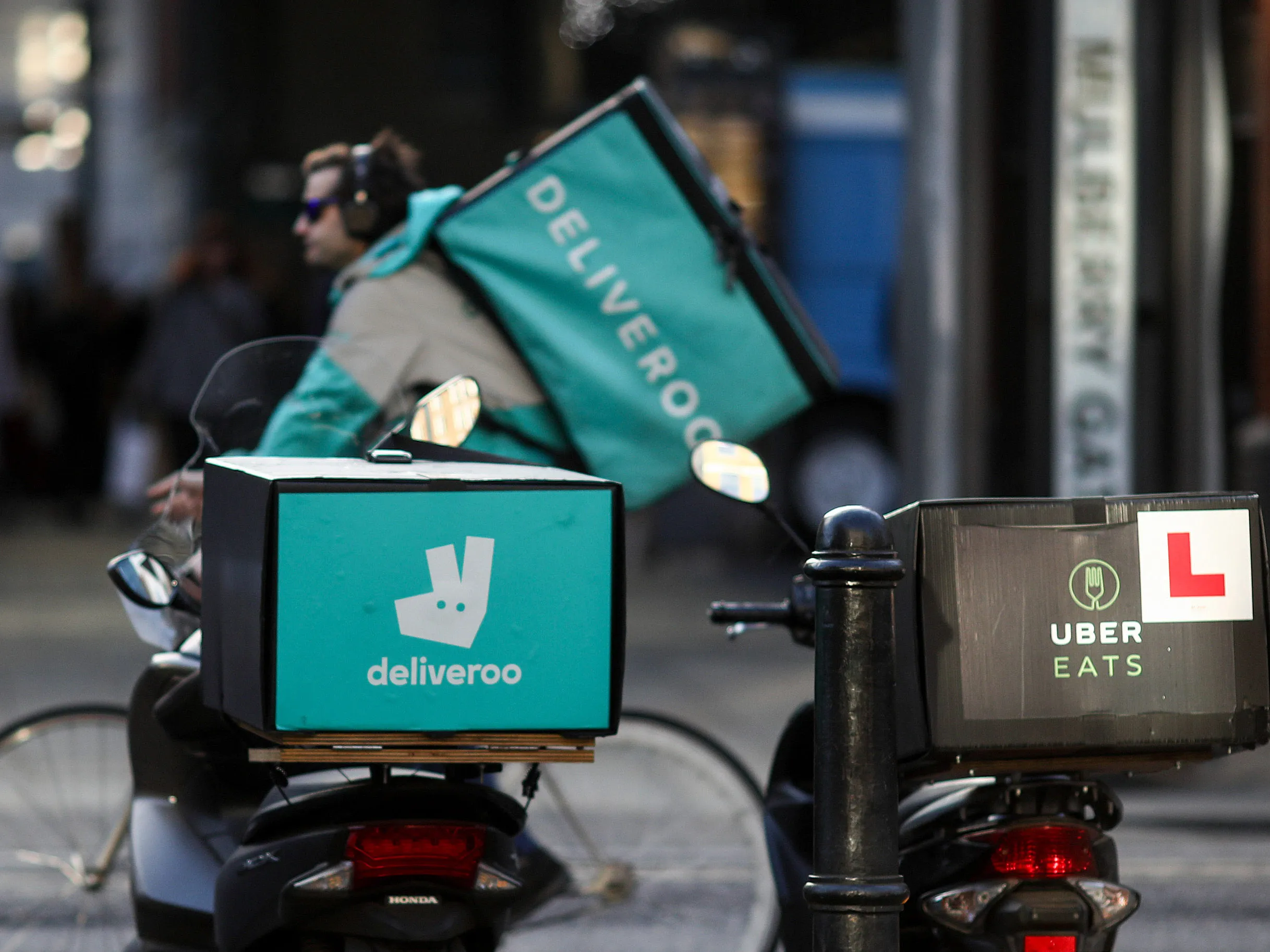 A food delivery cycle courier&nbsp;passes motor scooters with boxes for Deliveroo&nbsp;and UberEats&nbsp;in London.