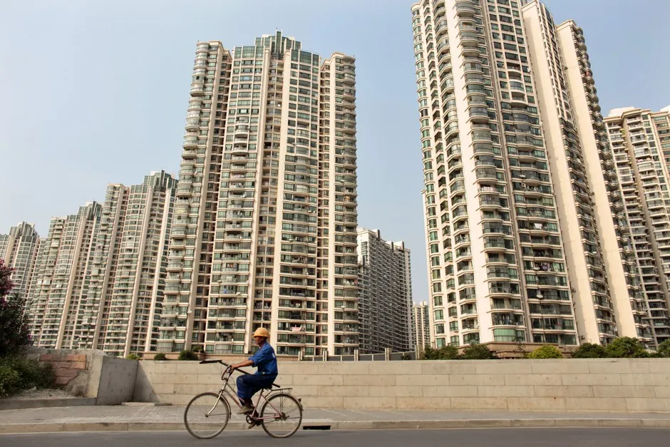 A migrant laborer rides a bicycle past a residential community in Shanghai.