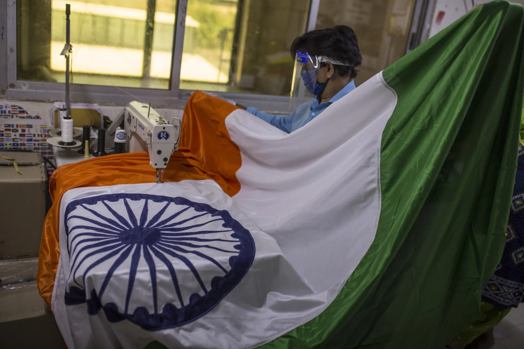 An employee wearing a protective face shield and mask sews a section of an Indian national flag at a workshop in Mumbai, India.