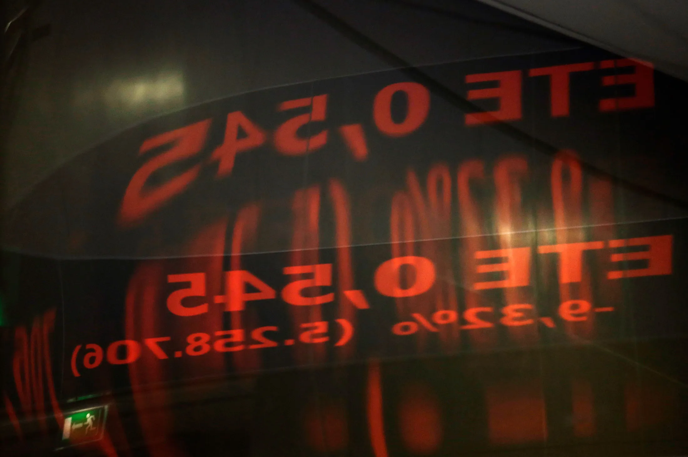 A reflection of share prices on an electronic ticker screen sits on a glass door panel inside the Athens Stock Exchange.
