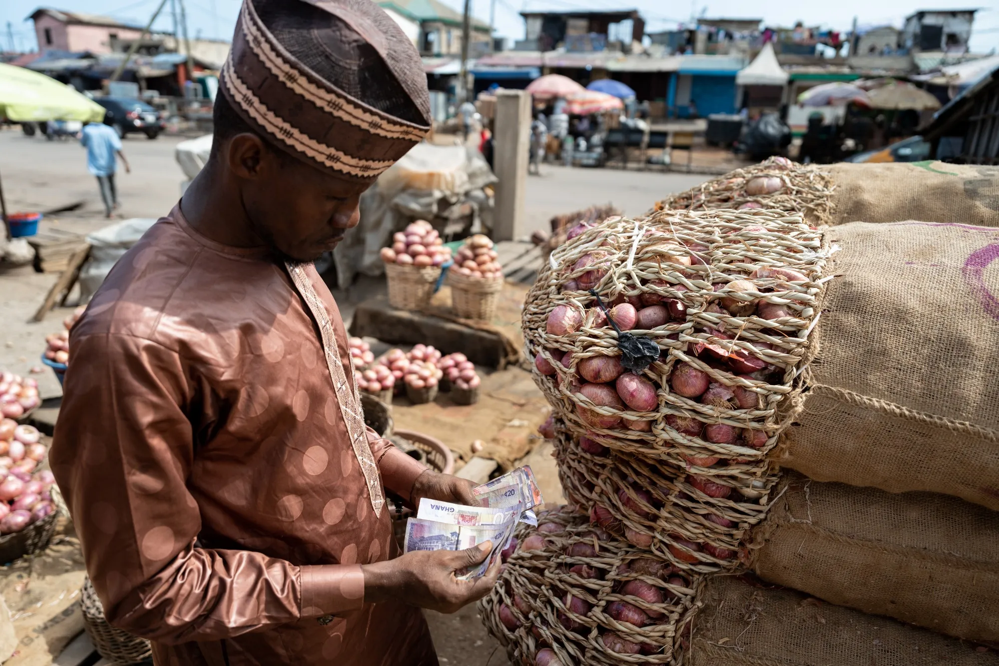 A trader counts Ghana cedi banknote by sacks of onions at a food market in Accra, Ghana.