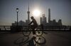 A man rides a bicycle along the Bund while buildings of Pudong's Lujiazui financial district stand across the Huangpu River as the sun rises in Shanghai, China, on Friday, Oct. 2, 2015. China's consumer inflation moderated and factory gate deflation extended a record stretch of declines, signaling the People's Bank of China still has room to ease monetary policy further to support a slowing economy.