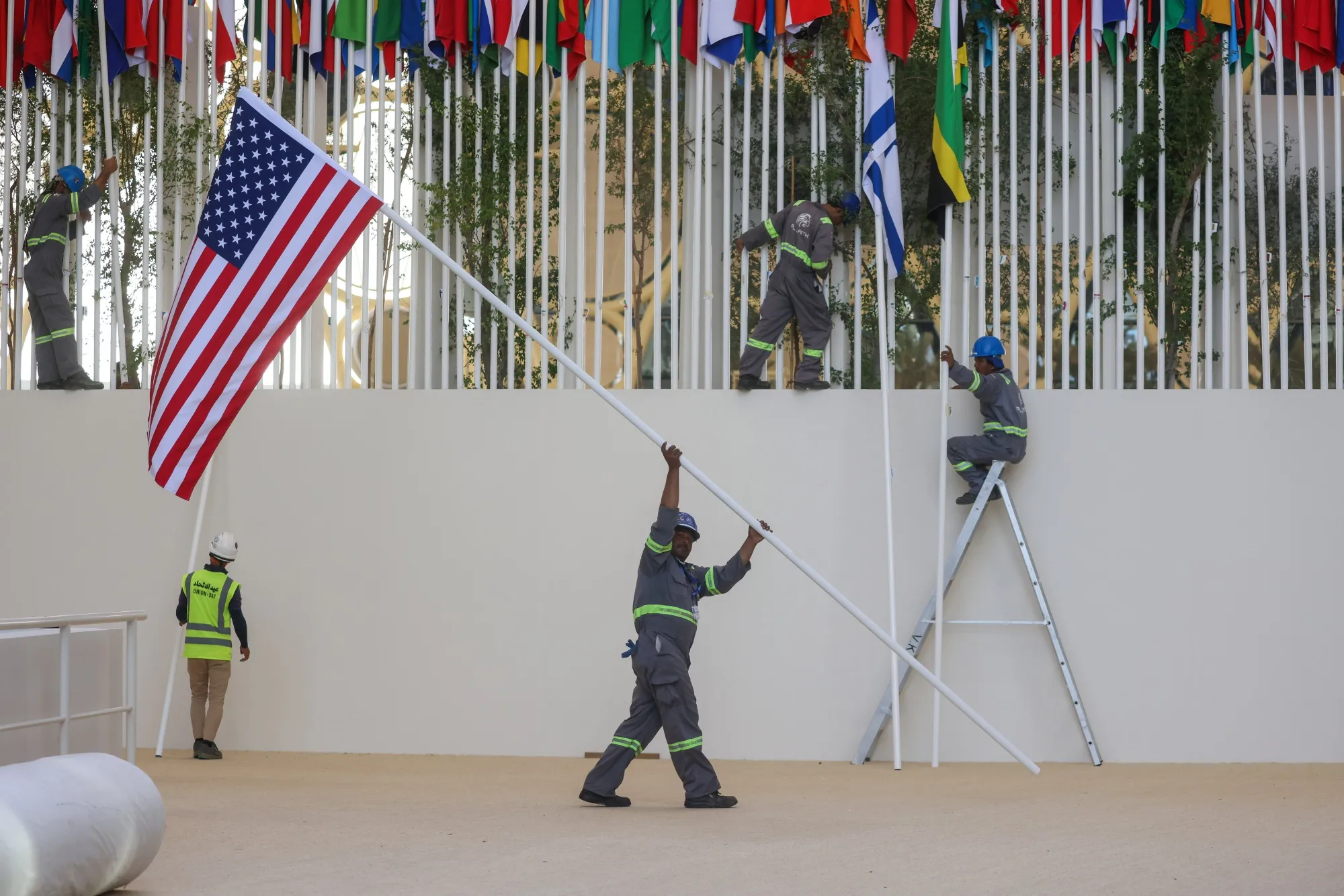 Workers erect national flags on the opening day of the COP28 climate conference at Expo City in Dubai, United Arab Emirates, on Nov. 30, 2023. More than 70,000 politicians, diplomats, campaigners, financiers and business leaders are in Dubai&nbsp;to talk about arresting the world’s slide toward environmental catastrophe.