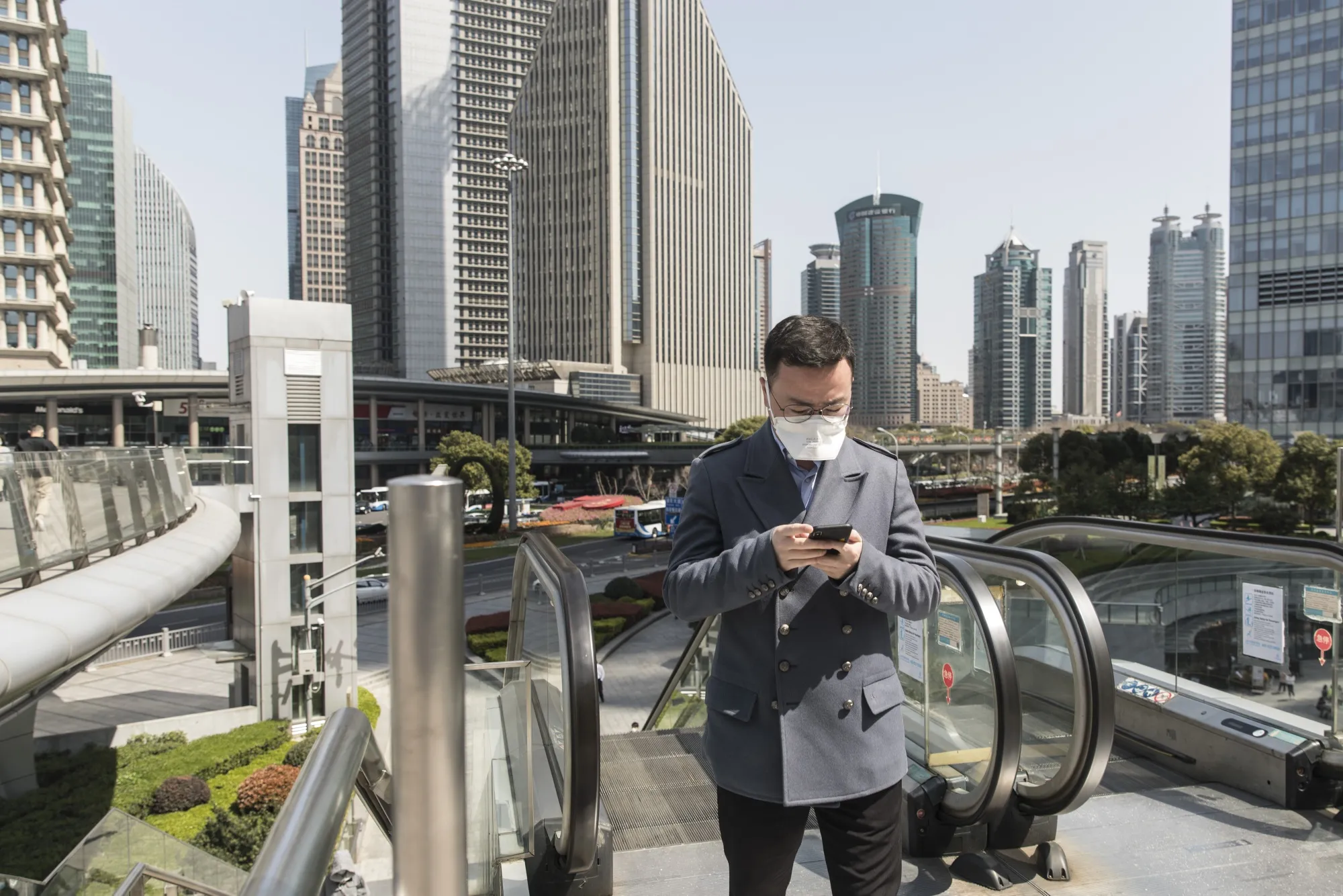 A pedestrian wearing a protective mask uses a smartphone in the Lujiazui Financial District in Shanghai.