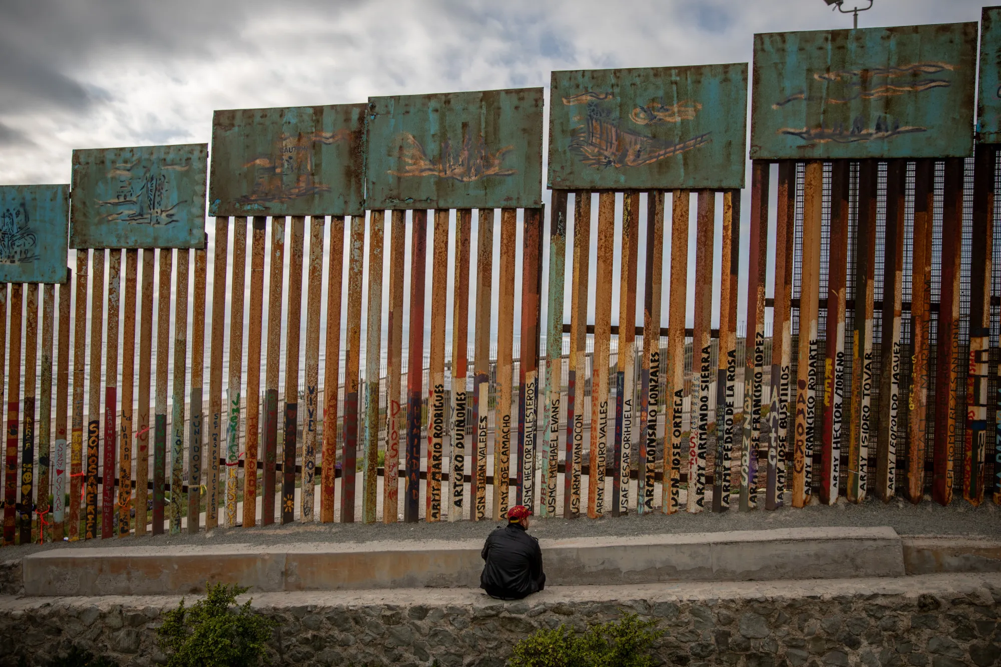 A person sits in front of a section of the U.S.-Mexico border wall in Tijuana, Mexico, on Saturday, May 19, 2018.