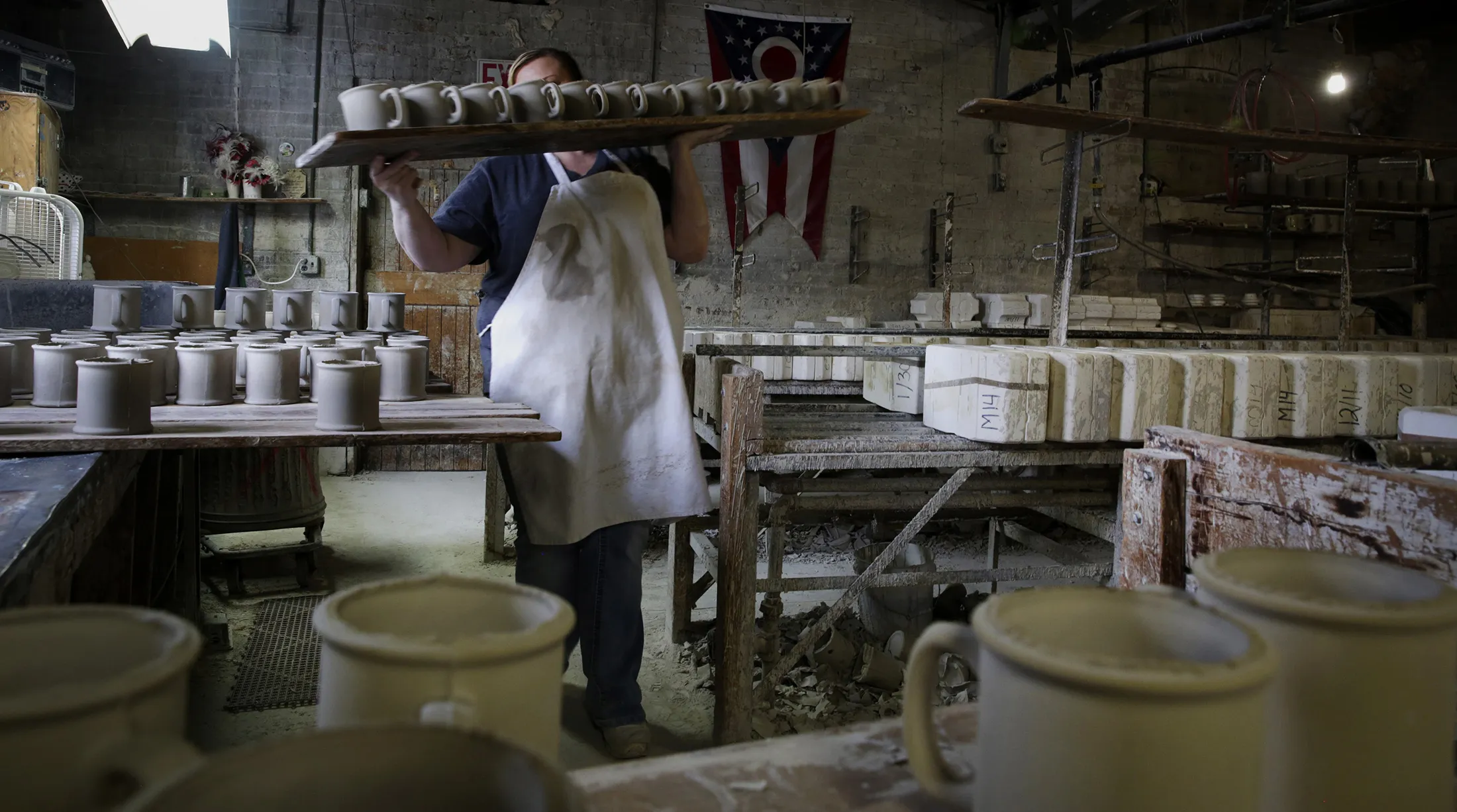 A worker carries a line of mugs to be polished before being fired in a kiln at a factory in East Liverpool, Ohio.