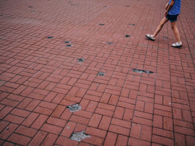 View of brick-tiled ground and a pedestrian's legs in Chernihiv’s central square. The ground has numerous pock-marked divets caused by the missile attack
