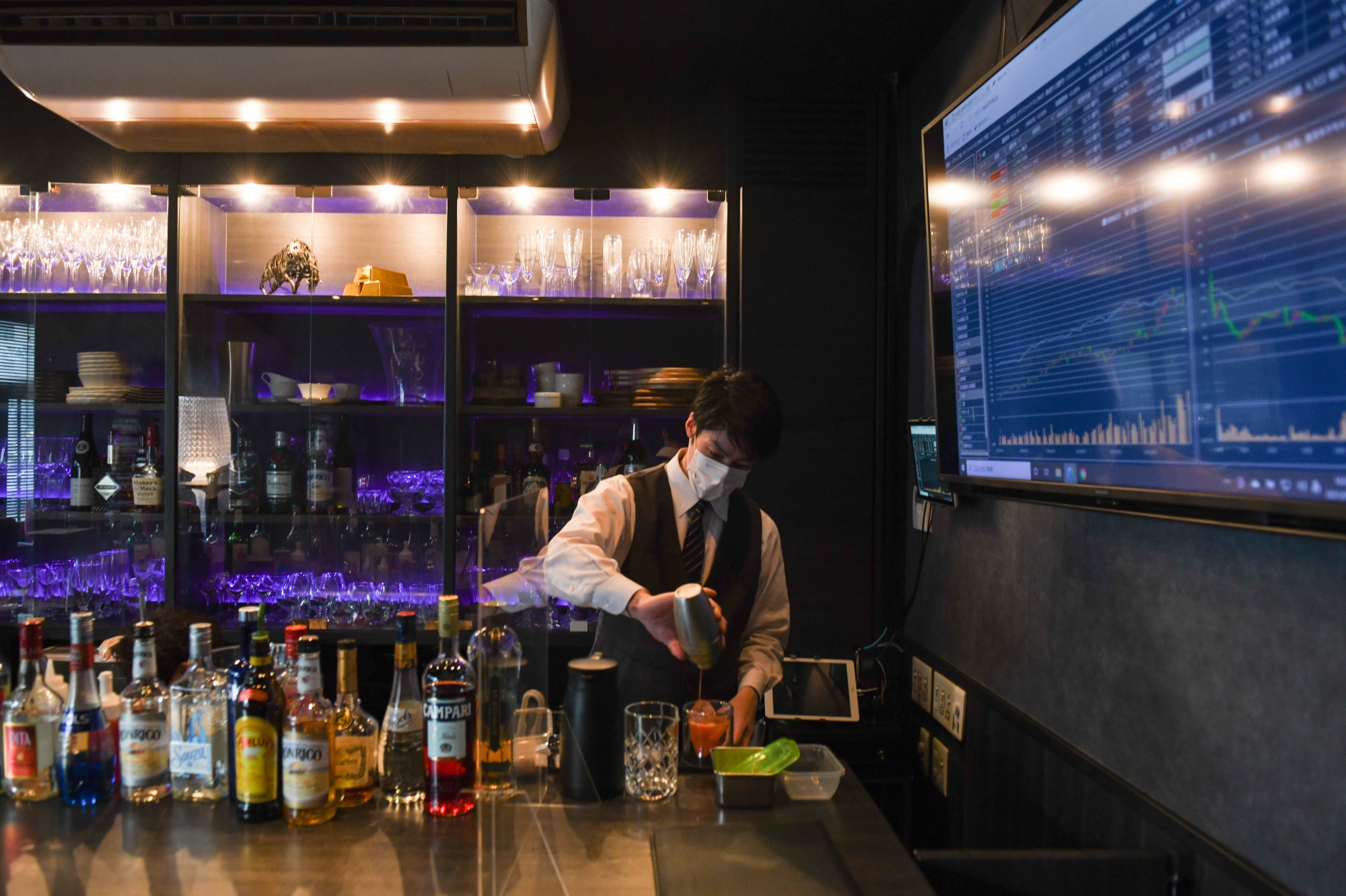 A bartender prepares drinks next to a screen displaying stock quotes and other financial information at Stock Pickers, a tip-trading bar for investors in the Ginza district of Tokyo, earlier in March.