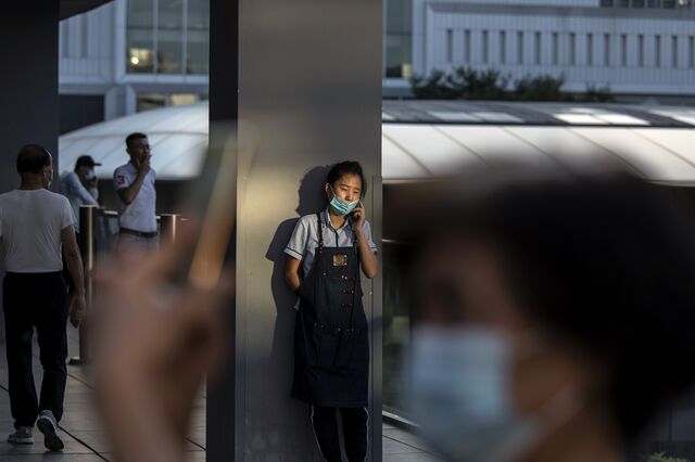 A worker talks on her mobile phone while taking a break in an upscale retail area in Beijing, China, on Wednesday, Aug. 25, 2021. China's Communist Party vowed to promote the welfare of all people and redistribute income, underscoring its push to achieve "common prosperity" in the country.