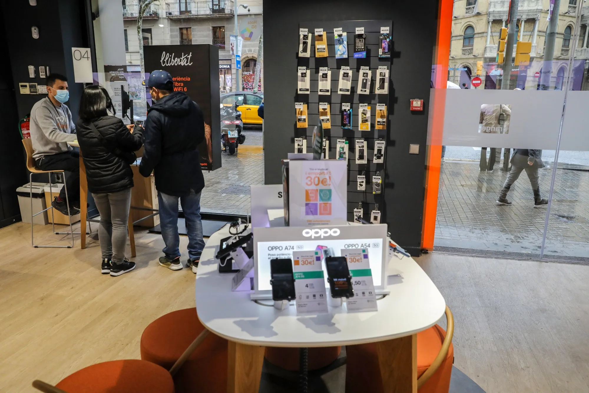 A retail assistant assists customers inside an Orange SA store in Barcelona, Spain.
