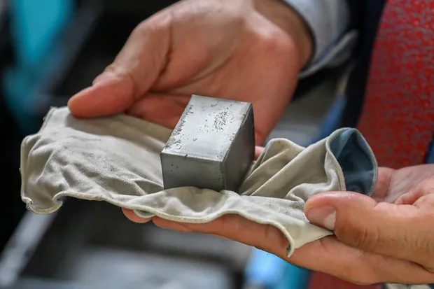Hands hold a rectangular rare earth magnet bar wrapped in cloth.