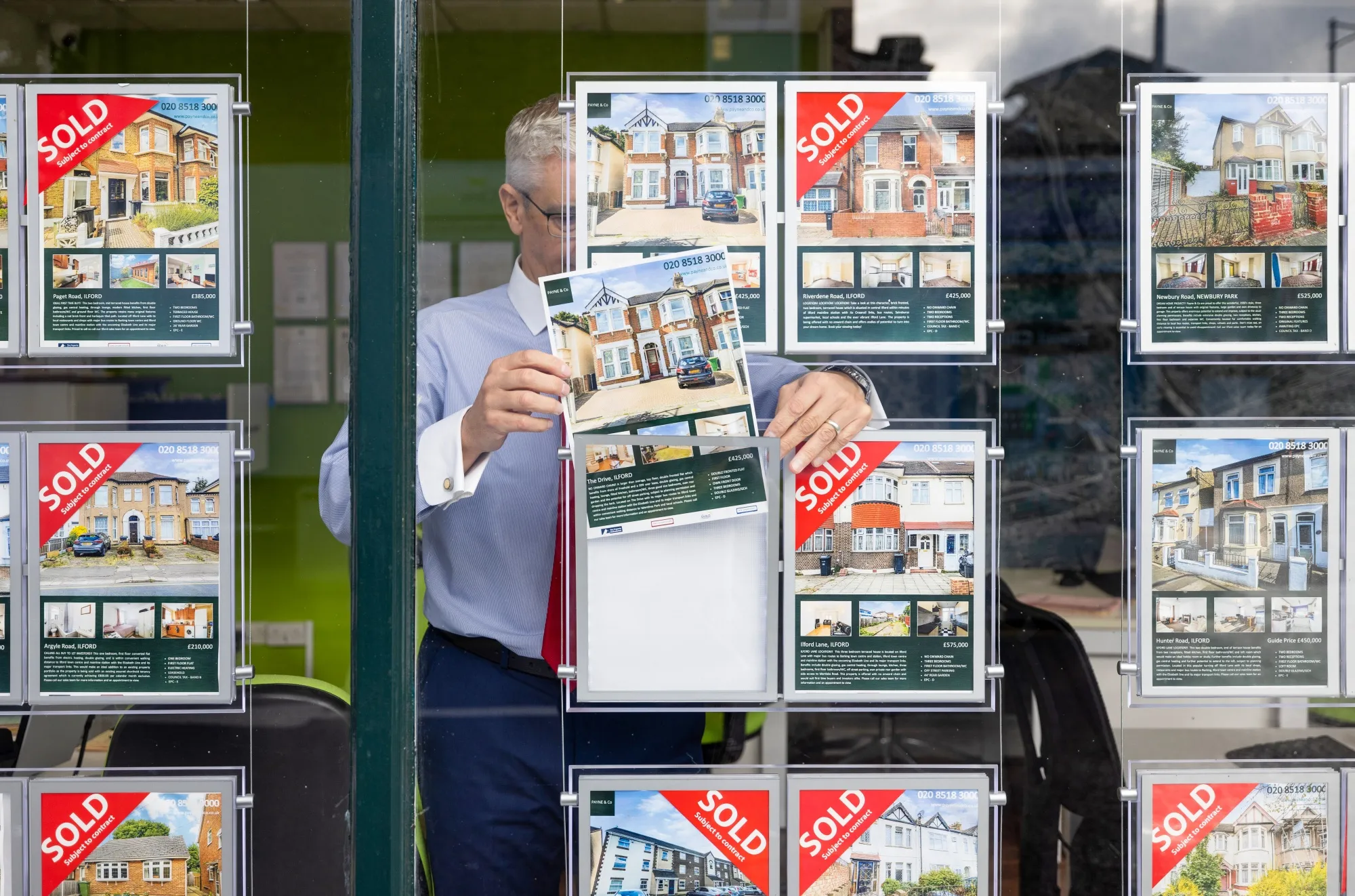An employee places a property for sale in the window of an estate agents in London, UK.