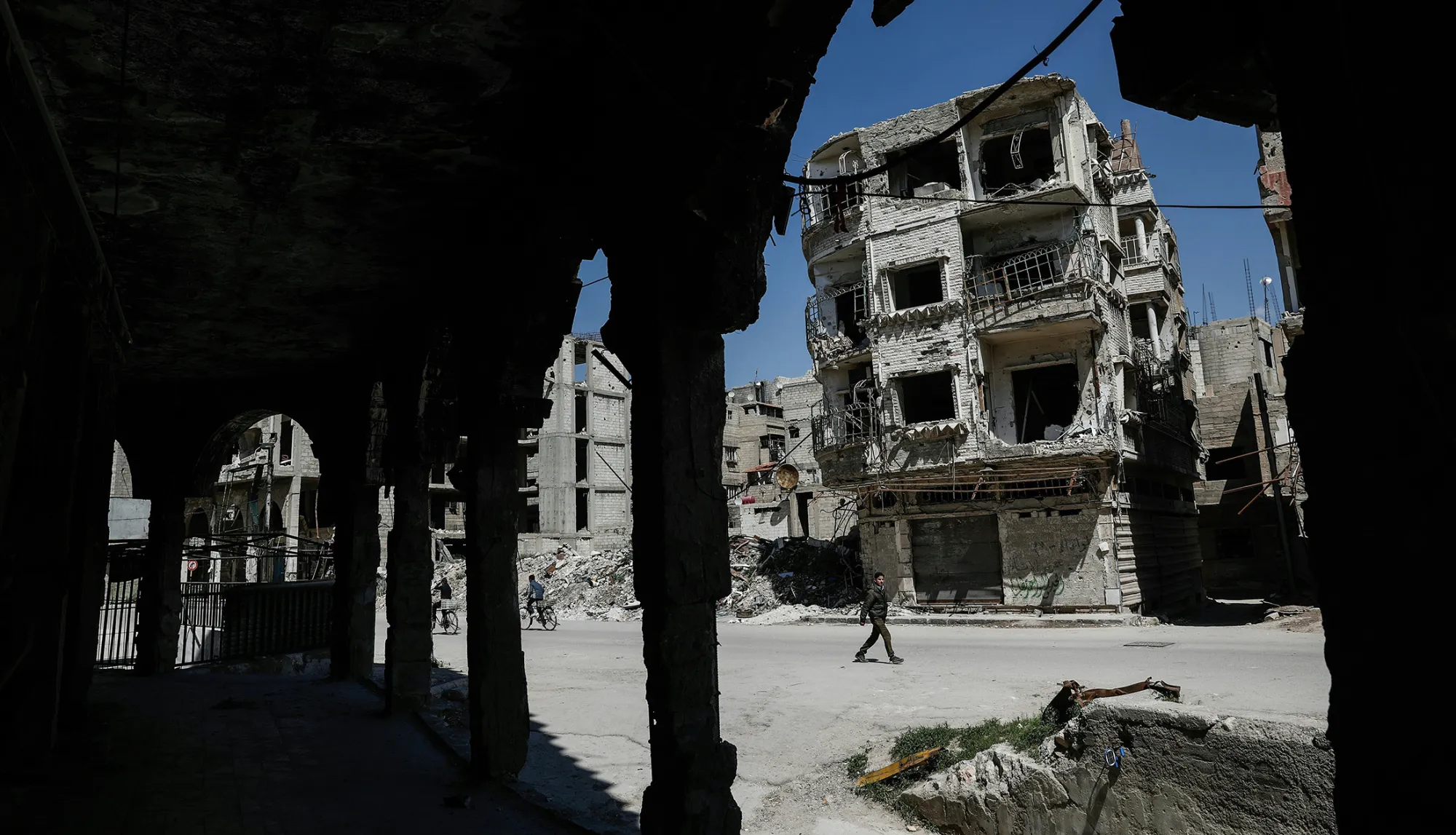 Syrians walk past damaged buildings on April 7, 2017, in the rebel-held town of Douma.
