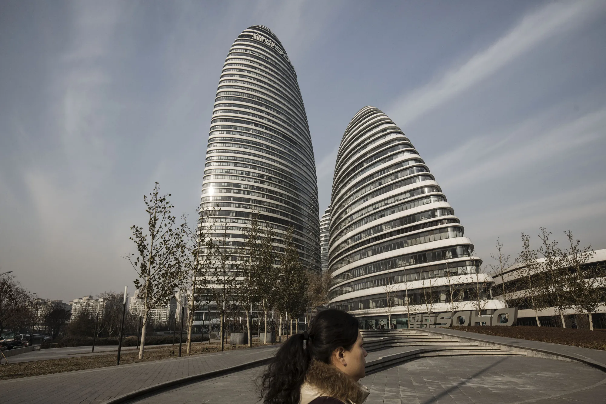A woman walks past commercial buildings at the Soho China Ltd. Wanjing Soho project in Beijing.