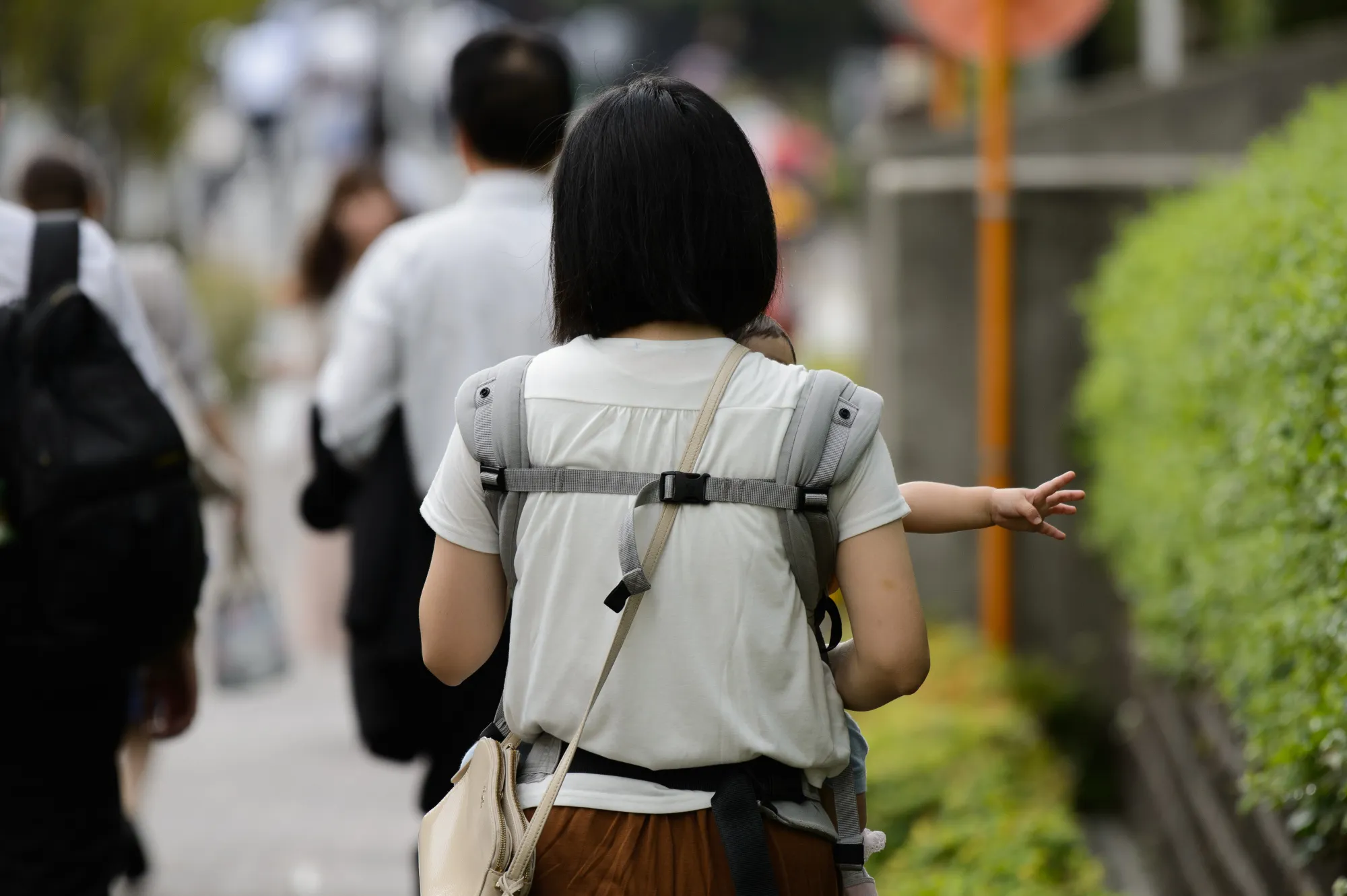 A woman carrying a baby walks along a sidewalk in Kawasaki, Kanagawa Prefecture, Japan.