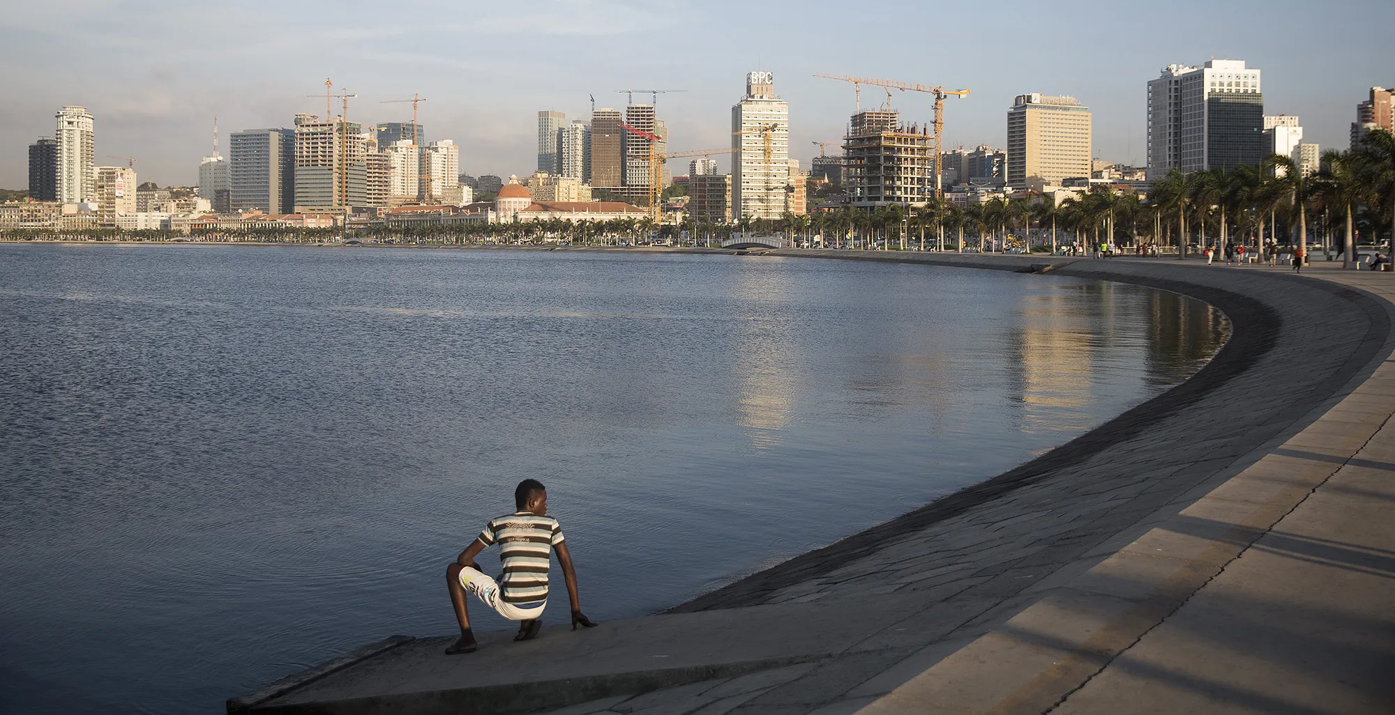 A person sits on the shoreline of&nbsp;the Bay of Luanda in Luanda, Angola.