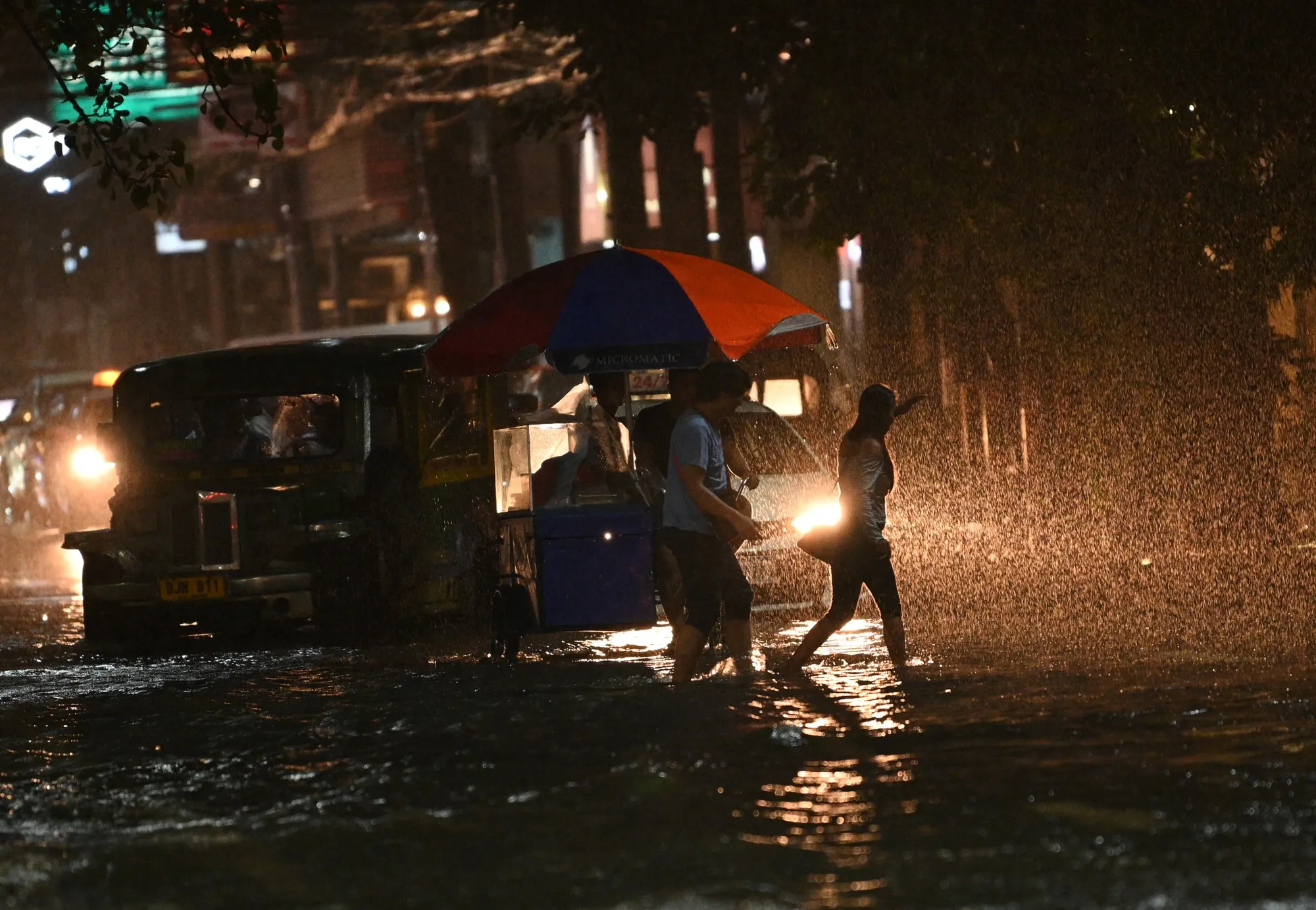 Pedestrians crossing through a flooded street of Manila as Tropical Storm Khanun intensifies the southwest monsoon rain on July 29.&nbsp;