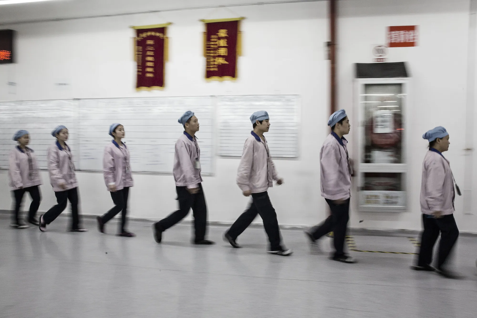 Employees make their way to the assembly line area after lining up for roll call at a Pegatron Corp. factory in Shanghai/&nbsp;