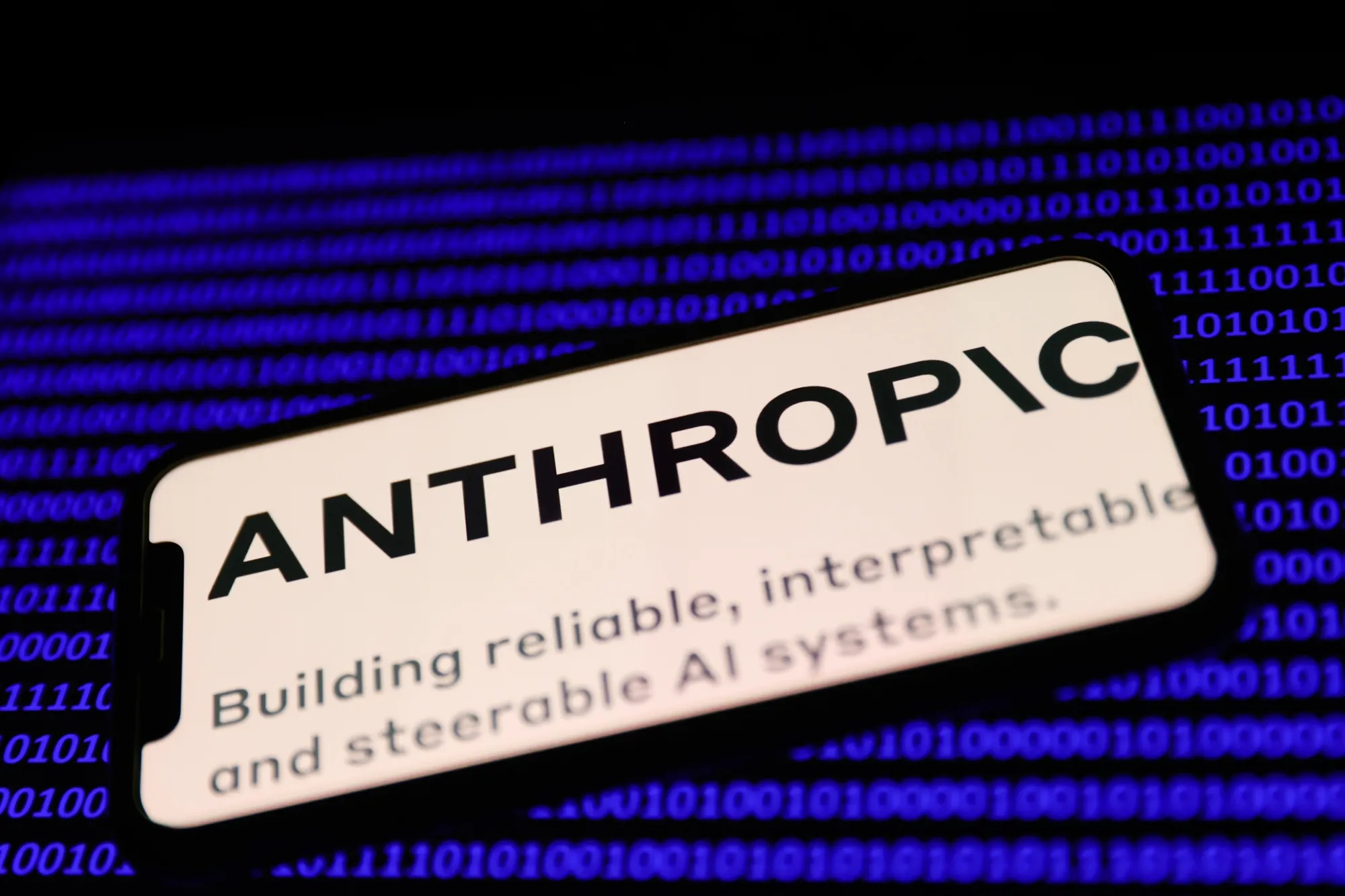 Anthropic logo displayed on a phone screen and a binery code displayed on a laptop screen are seen in this illustration photo taken in Krakow, Poland on February 7, 2023.&nbsp;