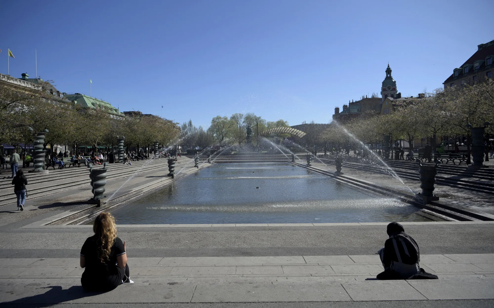 Pedestrians sit on steps by the fountains at the Kungstradgarden park in Stockholm on April 23.