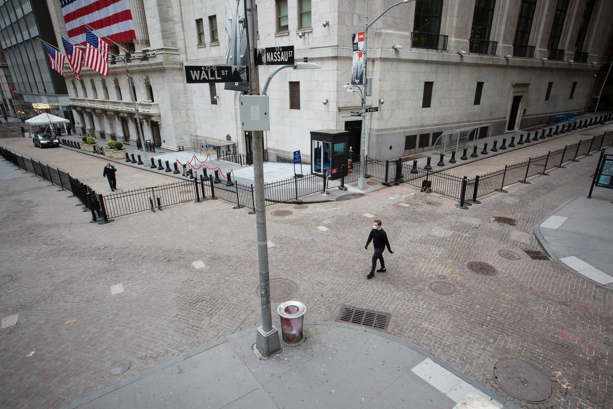 A pedestrian wearing a protective mask walks along Wall Street in front of the New York Stock Exchange in New York.
