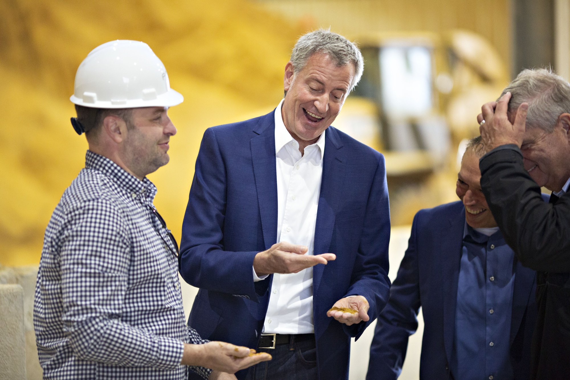 Bill de Blasio, center, smiles while holding a handful of dried distillers grains in Iowa.