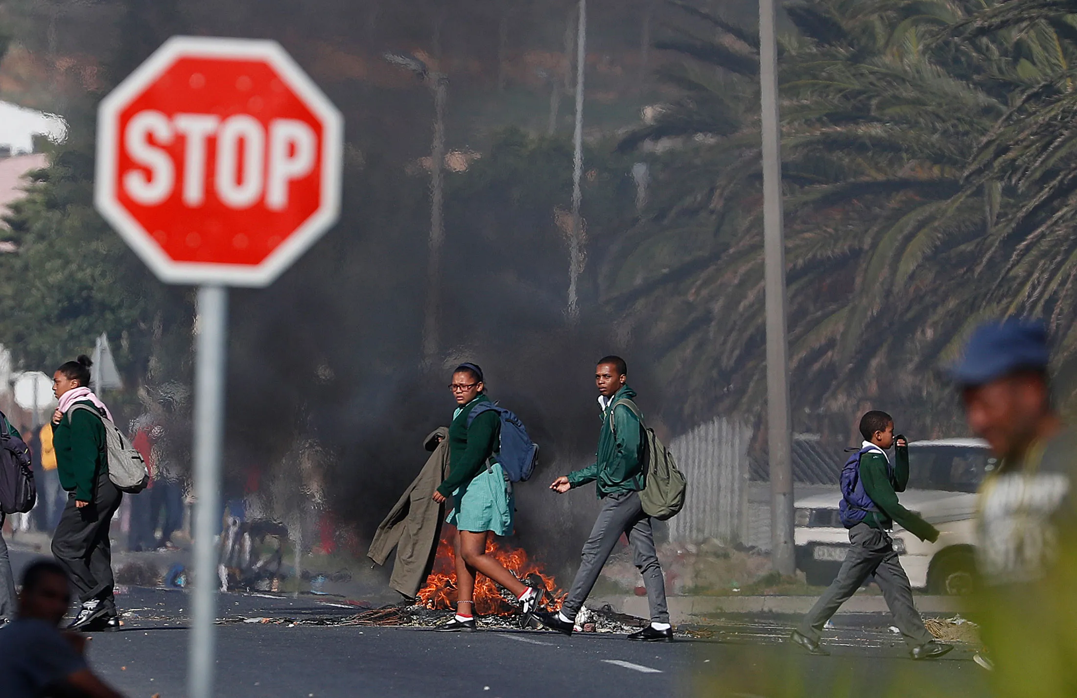 South African students on their way home from school walk past a burning barricade during protests in Cape Town.