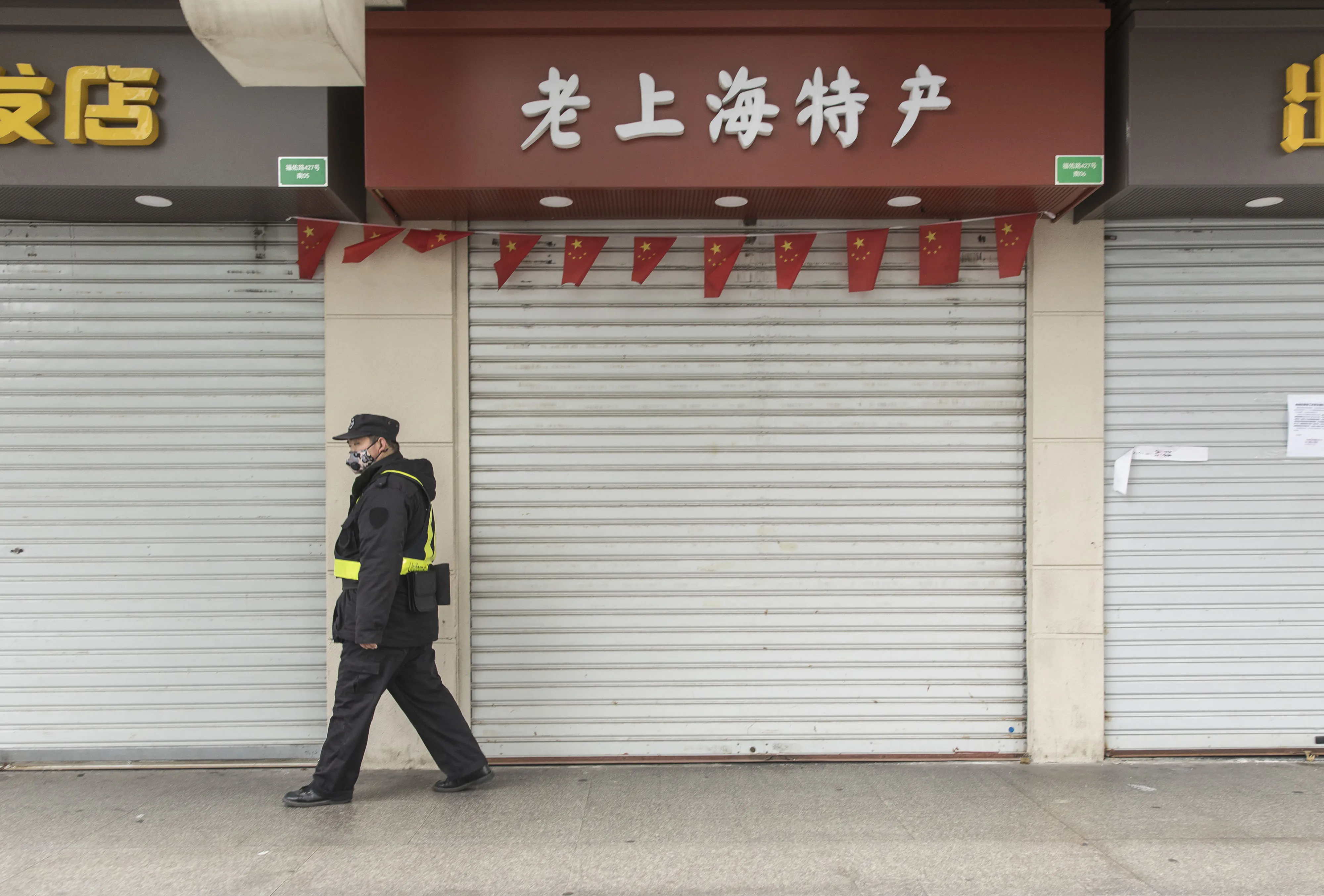 A security guard wearing a face mask passes shuttered retail stores at the Yuyuan Bazaar in Shanghai.
