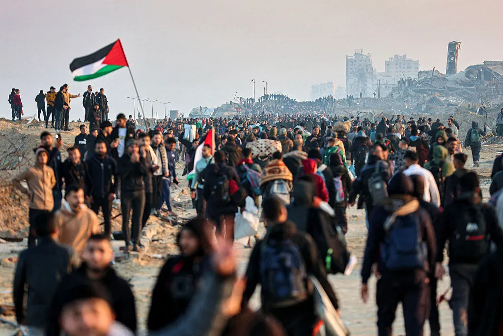 A Palestinian flag flies as people walk along Gaza's coastal al-Rashid Street to cross the Netzarim corridor from the southern Gaza Strip.