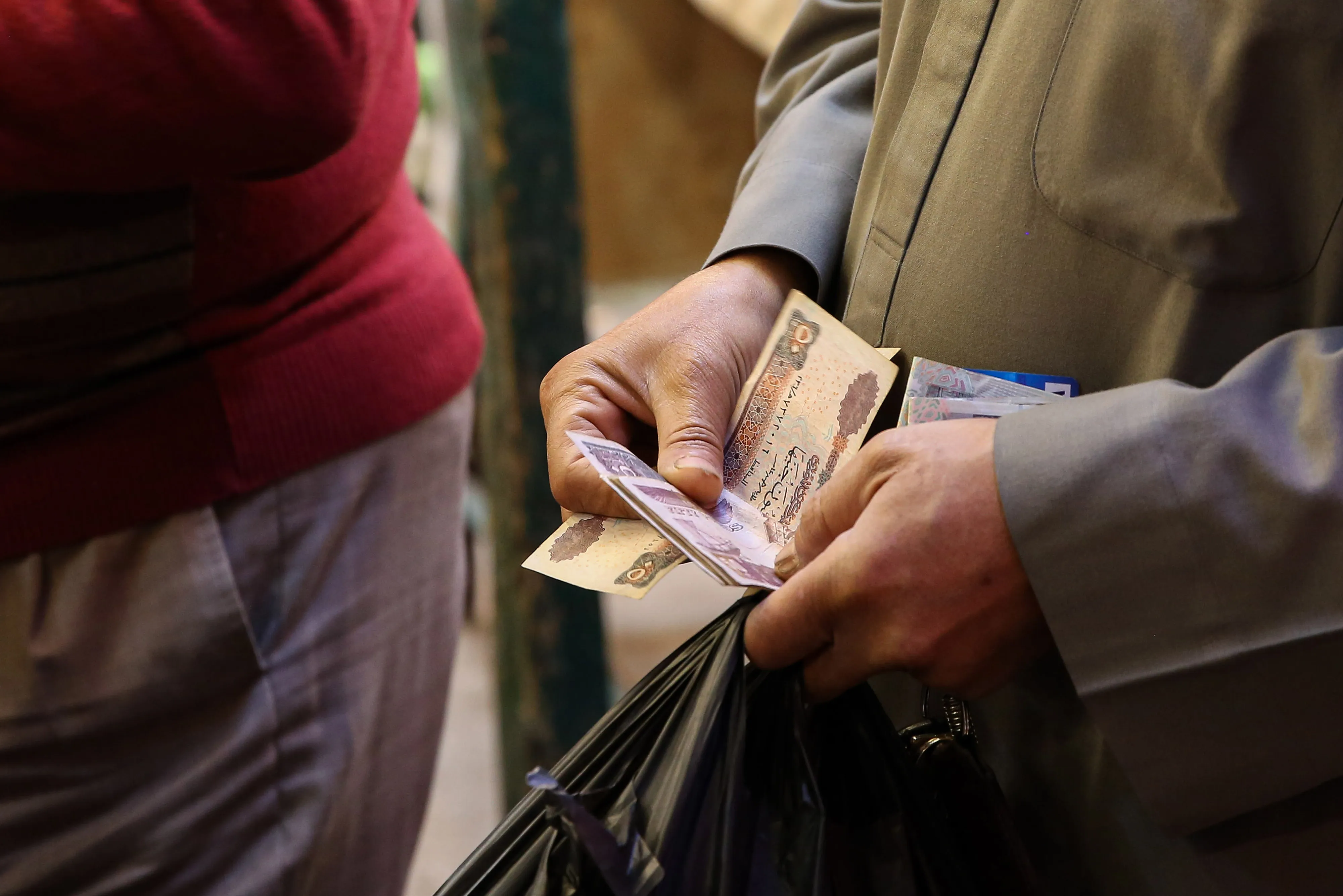 A customer holds Egyptian pound banknotes for a purchase at a food market in the Imbaba district of Giza, Egypt.