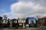 Houses marked for demolition stand next to a billboard advertising a future condominium to stand in their place in Toronto.