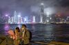 People adjust their hair and a protective mask while posing for a selfie photograph against the city skyline at night in the Tsim Sha Tsui district of Hong Kong, China, on Friday, Feb. 14, 2020. As fears of the novel coronavirus (Covid-19) spread across the region, pharmacies and supermarkets in Hong Kong are running out of basic supplies like toilet paper, paper towels, hand sanitizer and especially masks.