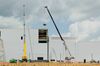 A photo of white buildings being constructed. There are construction cranes at work in the picture lifting materials up toward the construction.