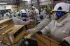 Workers at a factory working with machinery and moving boxes.