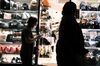 Pedestrians walk past a handbag store at night in the Shinjuku district of Tokyo, Japan.