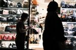 Pedestrians walk past a handbag store at night in the Shinjuku district of Tokyo, Japan.