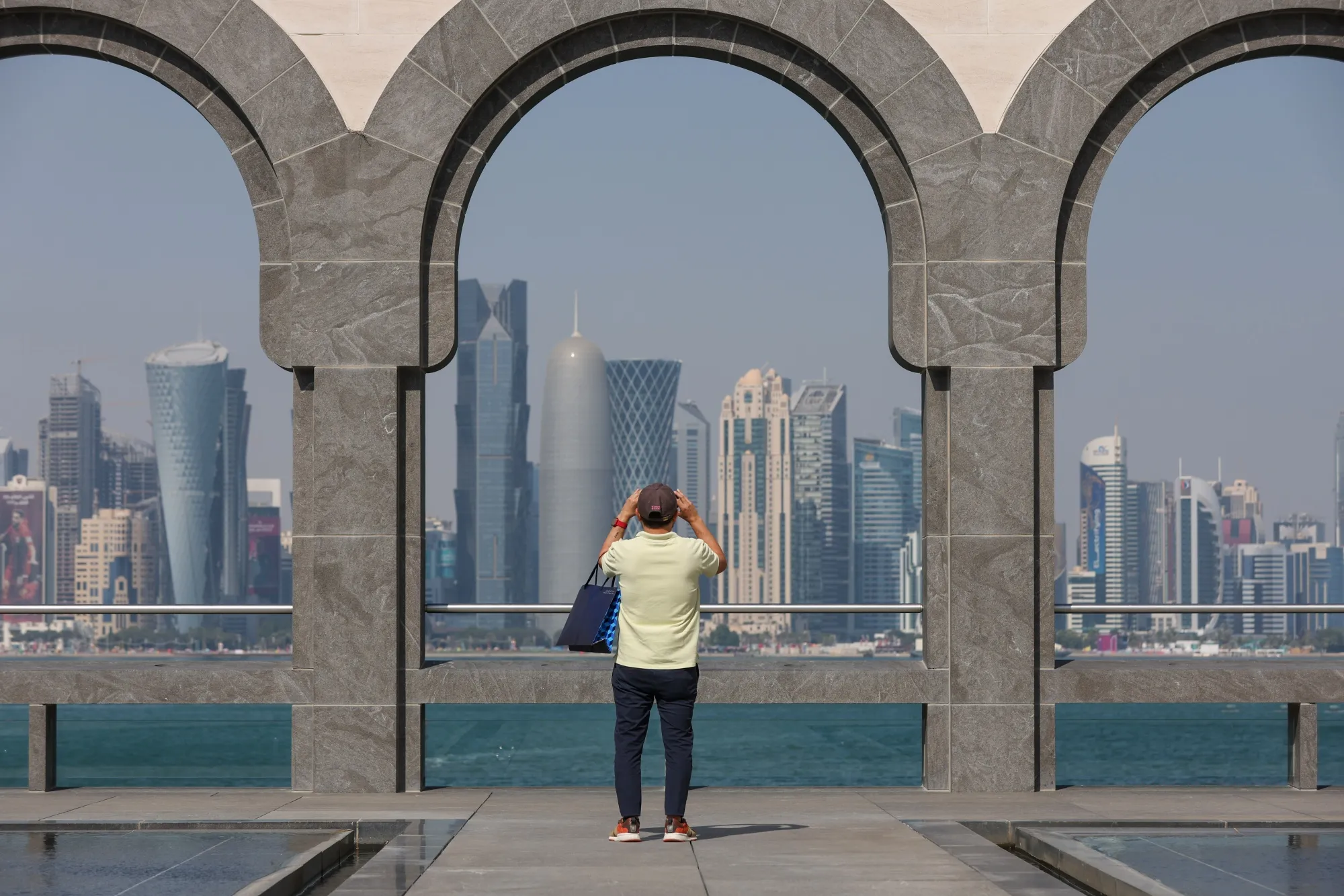 A tourist photographs residential and commercial skyscrapers in Doha, including the Qatar Financial Centre.