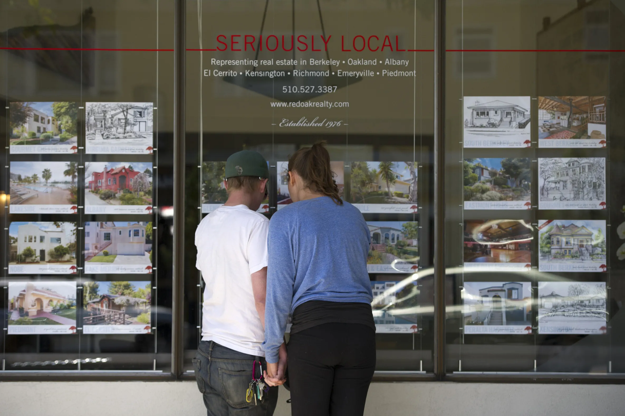 Pedestrians stop to look at flyers listing homes for sale at a realty office in Berkeley, California.