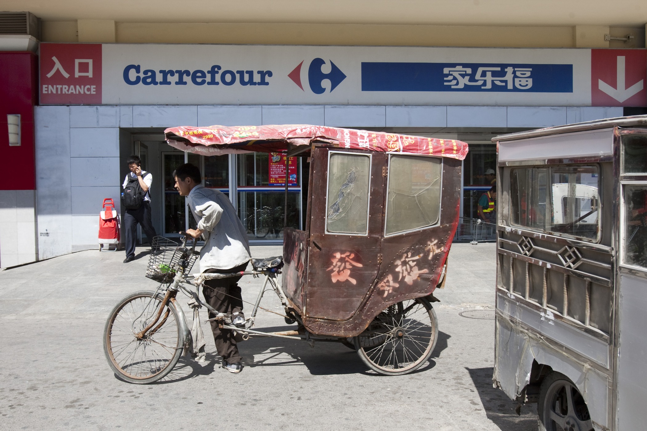 A bicycle taxi driver awaits customers outside a Carrefour SA store in Beijing.