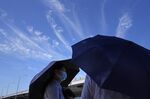 Residents cover up with umbrellas near a blue sky with wispy clouds during a hot day, Thursday, July 14, 2022, in Beijing. A heat wave is sweeping through parts of China. (AP Photo/Ng Han Guan)